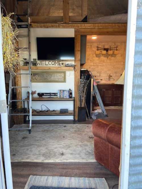 View from an entrance into a cozy interior with a welcome sign, a TV, and a kitchen area visible.