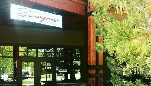 Sign for Beargrass Bistro in a modern building, framed by green pine branches.