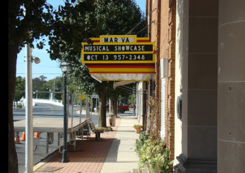 Sign for "Mar Va Musical Showcase" with date and phone number, displayed outside a brick building on a sunny day.