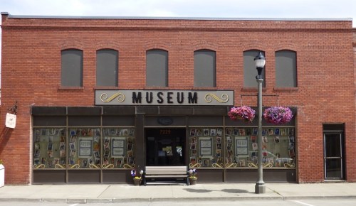 Front view of a brick museum building with large windows and flower baskets, featuring a sign that reads "MUSEUM."