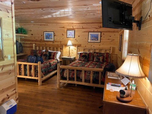 Cozy wooden cabin interior with two beds, a TV, and rustic decor, featuring warm lighting and a welcoming atmosphere.