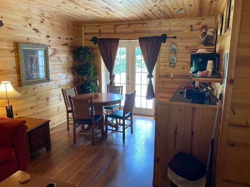 Cozy wooden cabin interior featuring a dining area, a red sofa, and large windows with curtains.