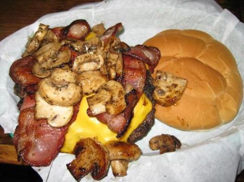 A hearty burger topped with sautéed mushrooms and bacon, served with a plain bun on the side.