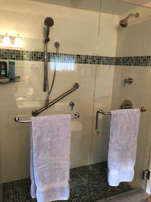 A modern shower with glass doors, featuring a handheld showerhead and two white towels hanging on bars.