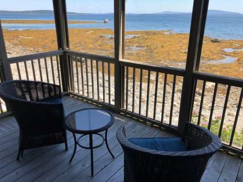 A cozy porch with two chairs and a table overlooking a rocky shoreline and calm water.