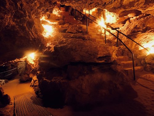Dimly lit cave interior with stone stairs and warm lights illuminating the rocky walls.