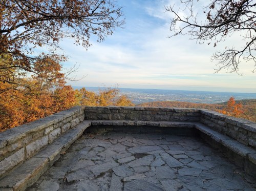 A stone overlook with a panoramic view of a valley and autumn trees under a clear sky.