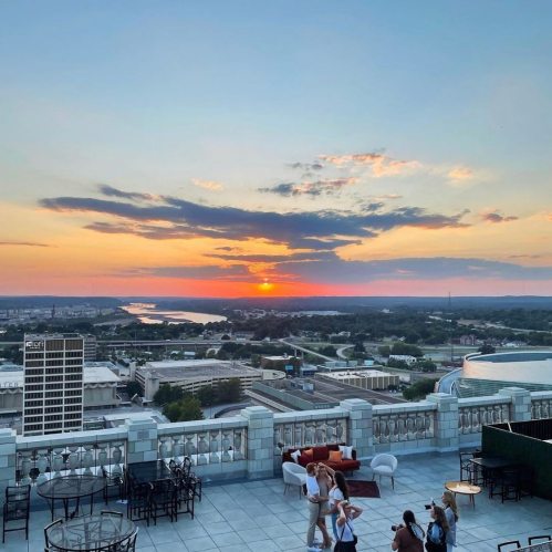 A sunset over a city skyline, with people enjoying the view from a rooftop terrace.
