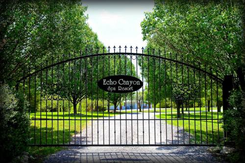 A wrought iron gate with "Echo Canyon Spa Resort" sign, surrounded by lush greenery and a gravel pathway.