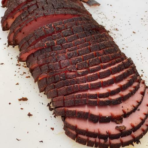 Sliced smoked meat with a dark, crispy crust and pink interior, arranged neatly on a white cutting board.