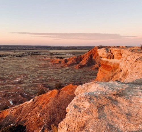 A scenic view of rugged red rock formations at sunset, with a vast landscape stretching into the distance.