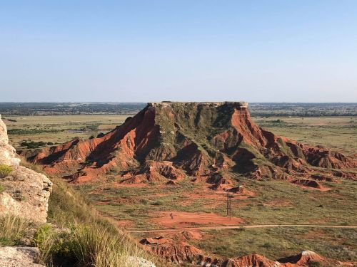 A scenic view of a red rock formation surrounded by green fields under a clear blue sky.