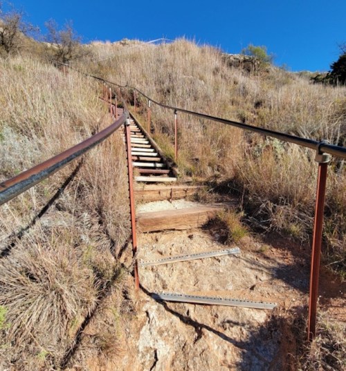 A winding staircase leads up a grassy hillside under a clear blue sky.