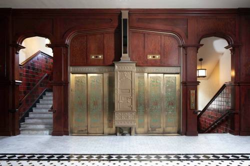 Elegant wooden elevator doors with intricate designs, flanked by a staircase in a vintage-style interior.