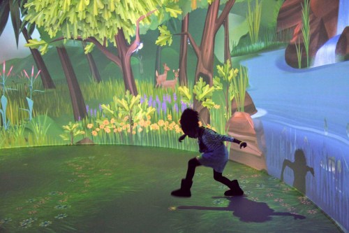 A child plays in a colorful, immersive forest environment with trees, flowers, and a stream.