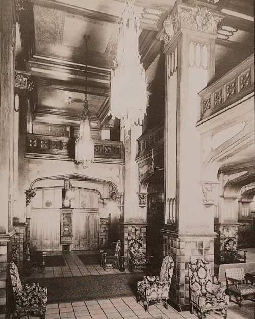 Historic interior of a grand lobby featuring ornate architecture, chandeliers, and elegant seating.