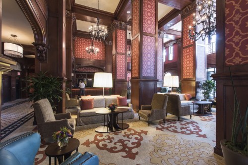 Elegant hotel lobby featuring plush seating, ornate decor, and large windows, illuminated by chandeliers.