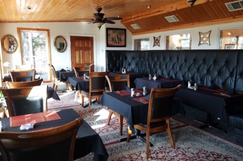 Cozy restaurant interior with black tables, leather seating, and wooden accents, featuring a warm, inviting atmosphere.