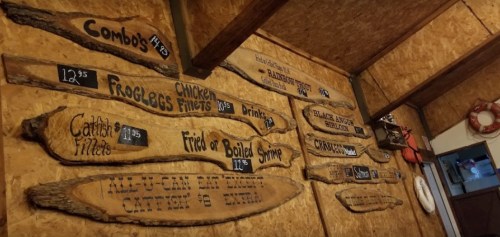 Wooden menu boards on a rustic wall display food and drink options with prices.
