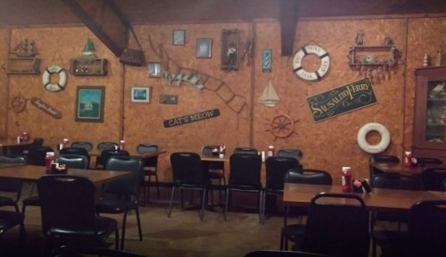 A rustic restaurant interior with wooden walls, nautical decor, and empty tables set for dining.