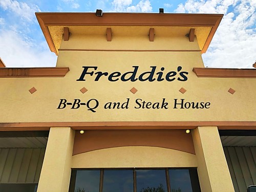 Sign for "Freddie's B-B-Q and Steak House" on a building with a blue sky in the background.