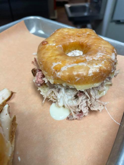 A glazed donut sandwich filled with pulled pork and melted cheese, resting on a tray with parchment paper.
