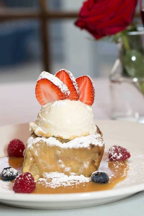 A warm dessert topped with strawberries and ice cream, surrounded by fresh berries and a drizzle of sauce.