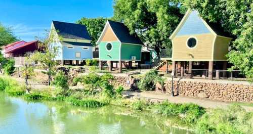 Colorful houses with unique designs by a serene waterway, surrounded by lush greenery and clear blue skies.