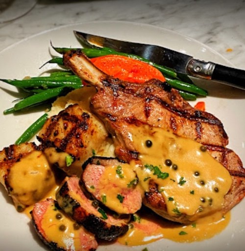A plate of grilled meat with a creamy sauce, served with green beans and a side of mashed potatoes.