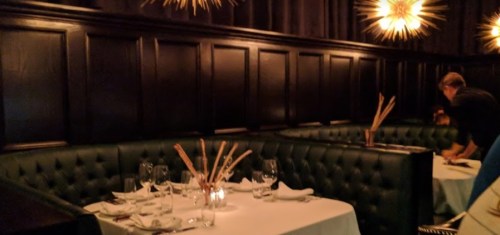 Elegant restaurant interior with dark walls, plush green seating, and stylish lighting. Tables set for dining.