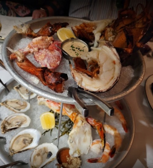 A seafood platter featuring lobster, crab, shrimp, and oysters on ice, garnished with lemon and dipping sauces.