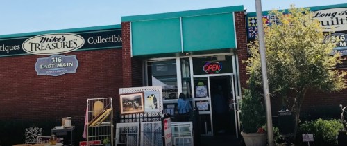 A storefront with a teal awning and "Open" sign, featuring antiques and collectibles outside.