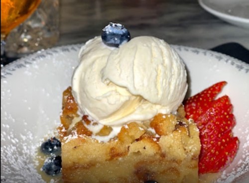 A slice of dessert topped with vanilla ice cream, blueberries, and strawberries, dusted with powdered sugar.