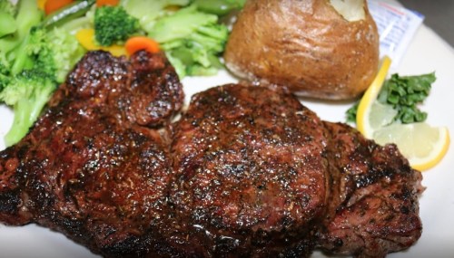 A plate featuring a grilled steak, baked potato, and a side of steamed broccoli and carrots, garnished with lemon.