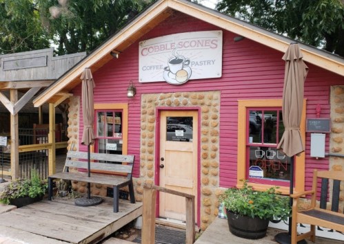 A cozy coffee and pastry shop with a pink exterior, wooden benches, and a welcoming sign that says "Open."
