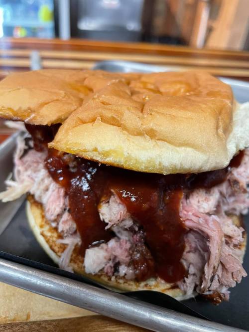 Close-up of a pulled pork sandwich with barbecue sauce on a soft bun, served on a metal tray.