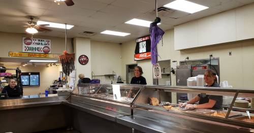 A barbecue restaurant with staff serving food at a counter, decorated for Halloween with a purple ghost.