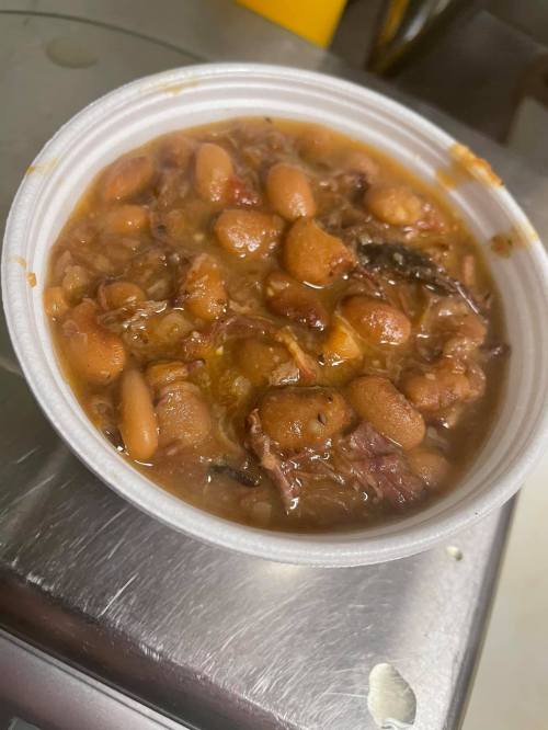 A white bowl filled with a hearty bean stew, featuring various beans and pieces of meat in a rich, brown sauce.