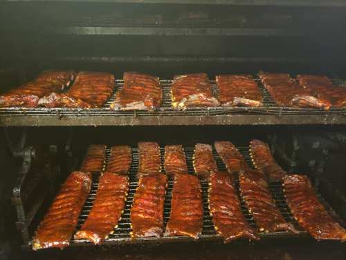 Racks of smoked ribs glistening with sauce inside a barbecue smoker.