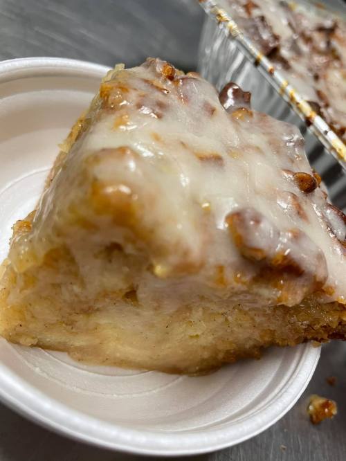 A slice of glazed dessert with a golden-brown crust, served in a white disposable cup.