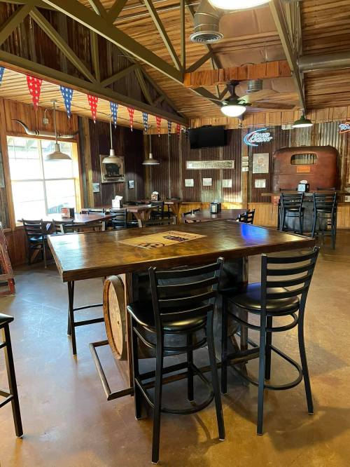 A rustic restaurant interior with wooden walls, a large table, and black chairs, decorated with red, white, and blue bunting.