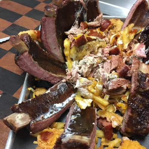 A platter of assorted meats, including ribs and pulled pork, served over a bed of fries and topped with barbecue sauce.