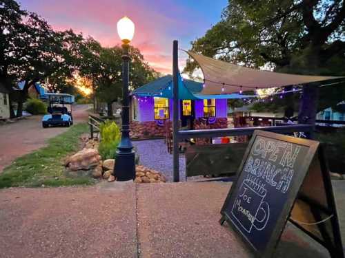 A cozy outdoor café with a "Open Brunch" sign, surrounded by trees and a colorful sunset in the background.