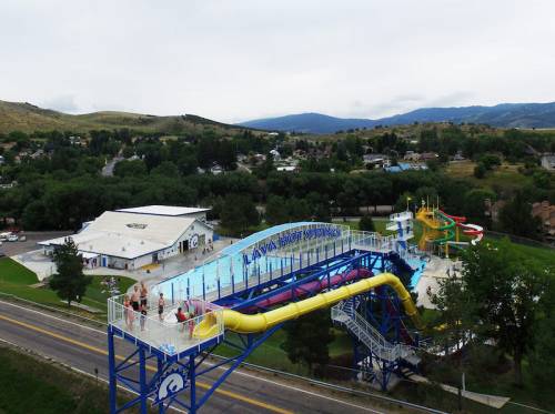 Aerial view of a water park featuring colorful slides, a large pool, and surrounding green hills.