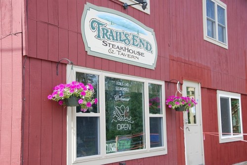 Sign for "Trail's End Steakhouse & Tavern" on a red building, with flower baskets and an "Open" sign in the window.