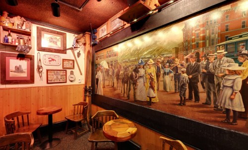 A cozy room featuring wooden tables, chairs, and a large mural depicting a historical street scene.