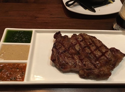 A grilled steak served on a white plate with three colorful sauces: green, brown, and orange.