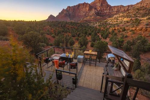 A scenic outdoor deck with seating and a view of mountains and trees at sunset.
