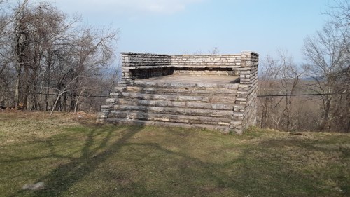 Stone platform with steps, surrounded by bare trees and grass, under a clear blue sky.