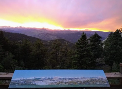 A panoramic view of mountains at sunset, with vibrant colors in the sky and trees in the foreground.